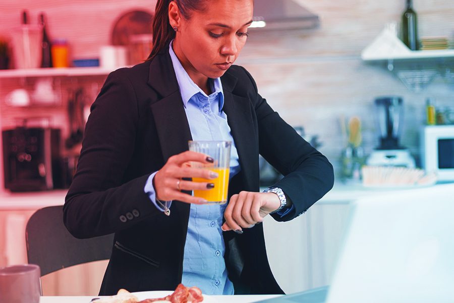 Mulher com copo de suco olhando para o relógio preocupada